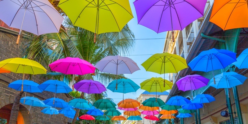 Colourful umbrellas sit on strings above the shoppers on Le Caudan Waterfront