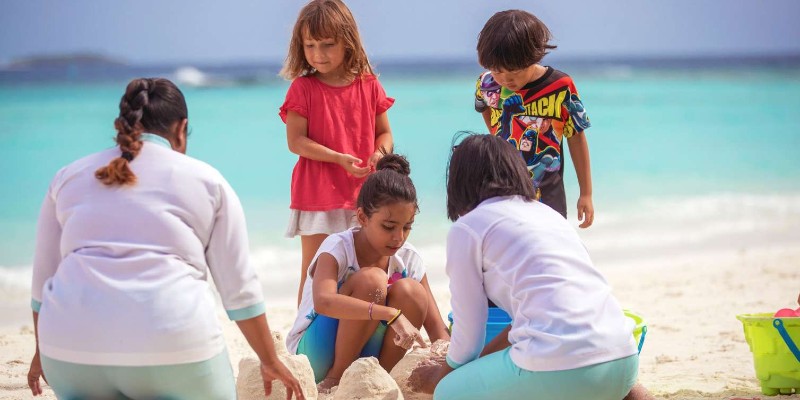 Koama Kid's Club staff help children playing in the sand