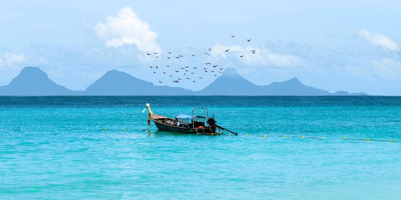 A boat with birds flying above it in the waters of Phang Nga Bay, Thailand