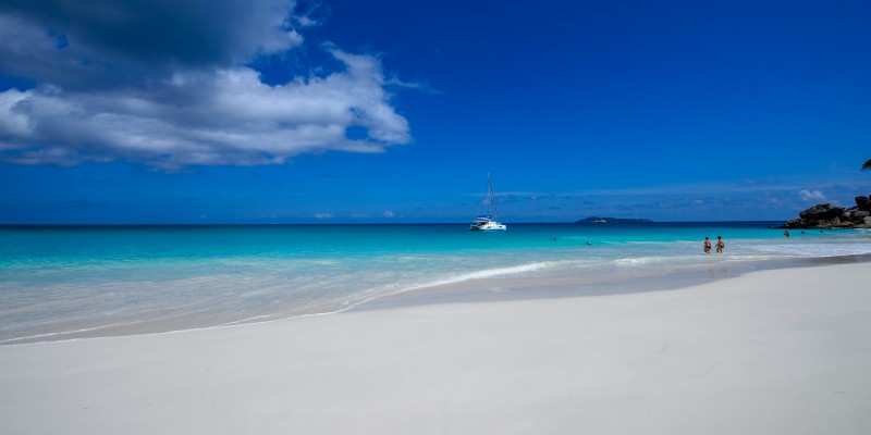 Some people and a boat rest in the Ocean water off a beach in Seychelles