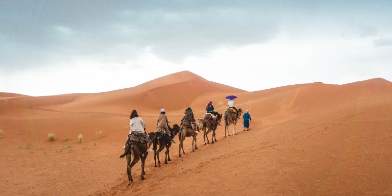 Five people ride camels through the desert in Dubai 