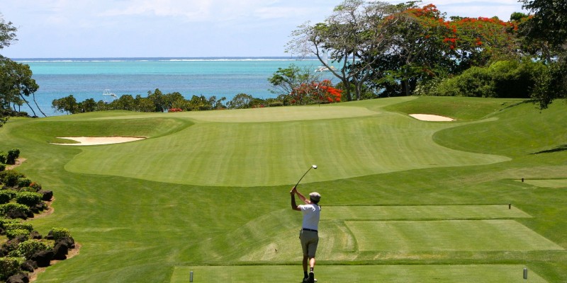 Man playing golf on a sunny course with the ocean in the background